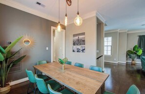 A dining area with a wooden table, teal chairs, hanging light fixtures, and a cityscape wall art. - Chic & Central 3-bd Townhouse, Mins to DT (Houston)