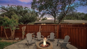 A backyard with a fire pit, four Adirondack chairs, a wooden fence, and trees. - Relaxing Texas Retreat, 4BR w Pool & Dream Kitchen (DeSoto)