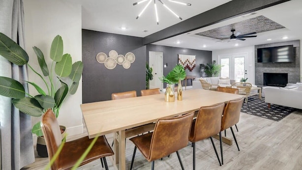 A modern dining area with a wooden table and brown chairs, a ceiling fan, and a TV in the background. - Relaxing Texas Retreat, 4BR w Pool & Dream Kitchen (DeSoto)