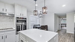 A modern kitchen with white cabinetry, a large island, stainless steel appliances, and pendant lighting. - 5-bd/2.5-ba Modern Farmhouse Retreat (Flower Mound)