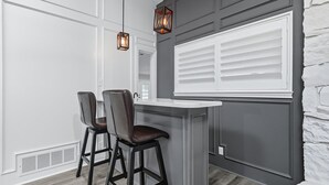 A kitchen with a central island, two bar stools, pendant lights, and a window with blinds. - 5-bd/2.5-ba Modern Farmhouse Retreat (Flower Mound)