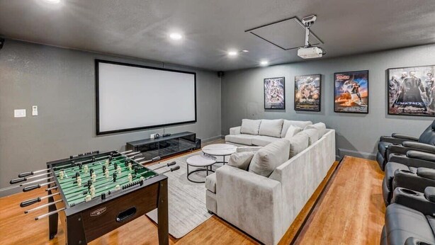 A room with a foosball table, a large screen, a sofa, and movie posters on the wall. - Texan 5/3 Oasis - Hot Tub, Pool, Cinema Room (Rowlett)