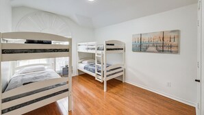 A bedroom with bunk beds, a ceiling fan, a beach-themed painting, and wooden flooring. - Texan 5/3 Oasis - Hot Tub, Pool, Cinema Room (Rowlett)