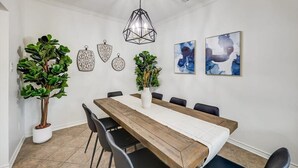 A dining area with a wooden table, black chairs, a white vase with flowers, and wall art. - Texan 5/3 Oasis - Hot Tub, Pool, Cinema Room (Rowlett)