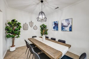 A dining area with a wooden table, black chairs, a hanging light fixture, and wall art. - Texan 5/3 Oasis - Hot Tub, Pool, Cinema Room (Rowlett)