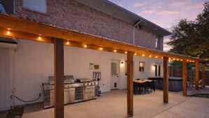 An outdoor patio with a grill, seating area, and string lights. - Texan 5/3 Oasis - Hot Tub, Pool, Cinema Room (Rowlett)