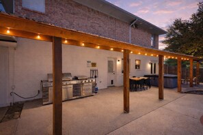 An outdoor patio with a grill, seating area, and string lights. - Texan 5/3 Oasis - Hot Tub, Pool, Cinema Room (Rowlett)