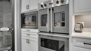 A kitchen with stainless steel appliances, including a microwave, oven, and refrigerator. There is a pantry door and a coffee maker on the countertop. - Clearview Castle - Pool, Jacuzzi, Lake View (Lewisville)