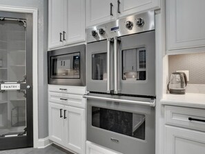 A kitchen with stainless steel appliances, including a microwave, oven, and refrigerator, with white cabinetry and a pantry door. - Clearview Castle - Pool, Jacuzzi, Lake View (Lewisville)