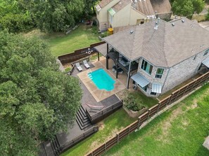 Eine Luftaufnahme eines Hauses mit Garten, das einen Swimmingpool, eine überdachte Terrasse und einen eingezäunten Deckbereich zeigt.