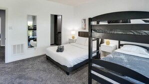 A hotel room with a bunk bed, a single bed, a mirror, a bedside table with a lamp, and a window with curtains. - Clearview Castle - Pool, Jacuzzi, Lake View (Lewisville)