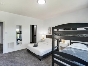 A hotel room with a bunk bed, a single bed, a mirror, a bedside table with a lamp, and a window with curtains. - Clearview Castle - Pool, Jacuzzi, Lake View (Lewisville)