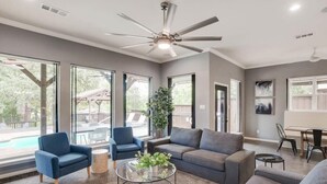 A spacious living room with a large window, a ceiling fan, and a pool visible outside. - Clearview Castle - Pool, Jacuzzi, Lake View (Lewisville)