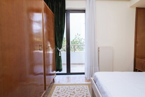 Ein Schlafzimmer mit Bett, Kleiderschrank, Heizkörper und Blick durch eine Glastür.