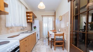 A kitchen with a stove, sink, wooden cabinets, and a dining area with a table and chairs. - Stylish and comfortable apartment 2 minutes from the beach (Kos)