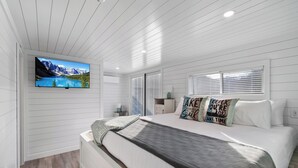 A modern bedroom with a large bed, a mounted TV, and a view of a mountain lake. - Dock Holiday - Unique Floating House on Cumberland (Russell Springs)