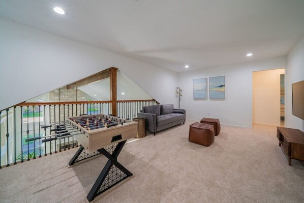 A spacious living area with a foosball table, a gray sofa, and a staircase leading to an upper level. - Bright and Spacious Home for w Pool -over 30 Nights- (Houston)
