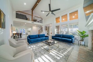 A spacious living room with a high ceiling, a ceiling fan, and a staircase leading to an upper level. - Bright and Spacious Home for w Pool -over 30 Nights- (Houston)