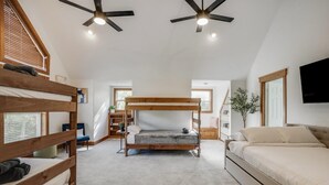 Quarto com uma cama de solteiro, uma cama de casal, um ventilador de teto e uma TV fixada na parede.