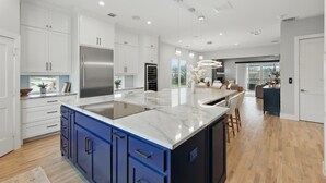 A modern kitchen with white cabinets, a large island, and a stainless steel refrigerator. - Luxury Living at its Finest 3bd/3.5ba (Flower Mound)