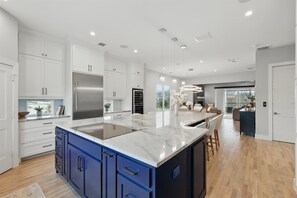 A modern kitchen with white cabinets, a large island, and a stainless steel refrigerator. - Luxury Living at its Finest 3bd/3.5ba (Flower Mound)