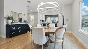 A modern dining area with a wooden table, white chairs, a dark console, and a large window. - Luxury Living at its Finest 3bd/3.5ba (Flower Mound)