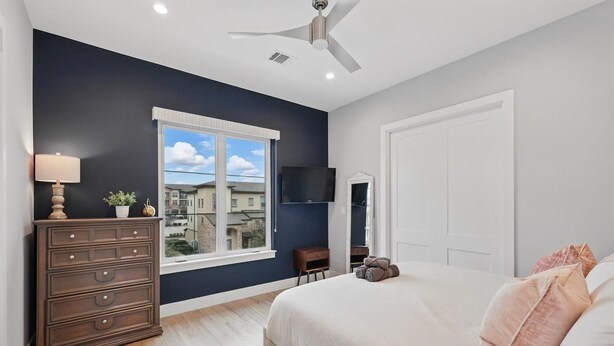 A bedroom with a bed, dresser, TV, and window with a city view. - Luxury Living at its Finest 3bd/3.5ba (Flower Mound)