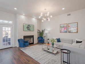 A modern living room with a fireplace, blue armchairs, a white sofa, and abstract art on the walls. - 5BD Glamorous Home Backyward Oasis, Cinema Room (McKinney)