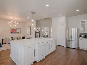 A modern kitchen with white cabinetry, a large island, stainless steel appliances, and a dining area with a sofa and artwork. - 5BD Glamorous Home Backyward Oasis, Cinema Room (McKinney)