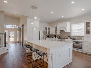 A spacious kitchen with white cabinetry, a large island, and bar stools. - 5BD Glamorous Home Backyward Oasis, Cinema Room (McKinney)