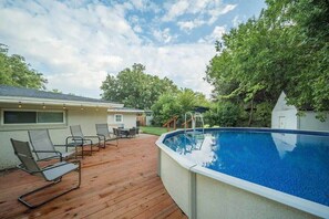 Ein Pool im Freien mit Holzterrasse, Liegestühlen und einem kleinen Haus im Hintergrund.