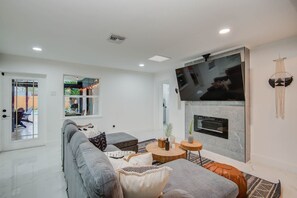 Ein modernes Wohnzimmer mit grauem Sofa, einem Flachbildfernseher über einem Kamin und einem großen Fenster.