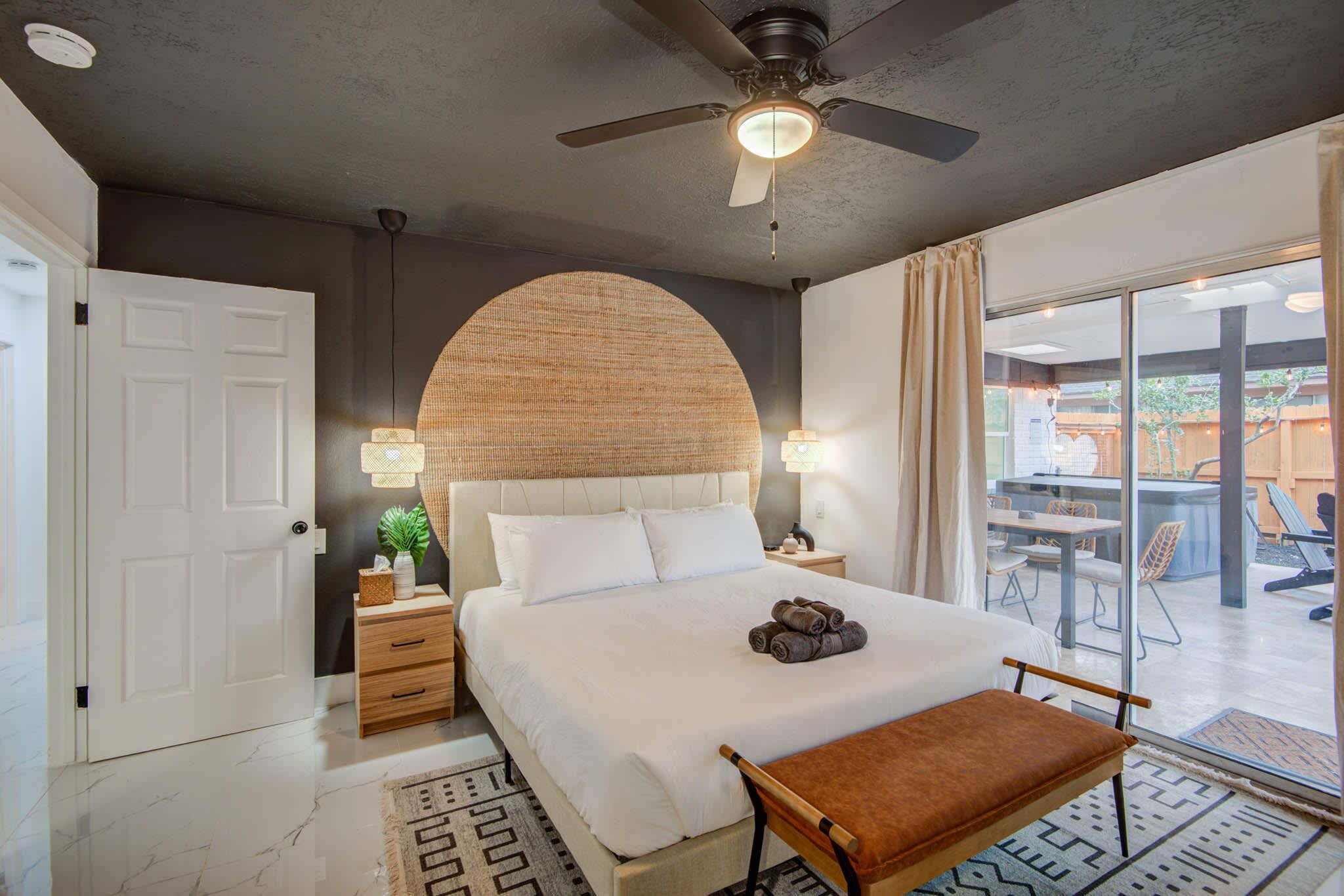 A bedroom with a bed, bedside tables, a ceiling fan, and a view of an outdoor patio.