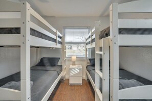 Une chambre avec un lit superposé, une table de chevet au centre, une fenêtre avec des stores et une vue sur l’extérieur.