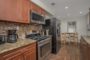 Eine moderne Küche mit Holzausstattung, einem Edelstahlherd, einem schwarzen Kühlschrank und einer Arbeitsplatte aus Granit.