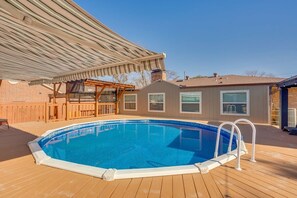 Ein Schwimmbad mit Holzterrasse, einer überdachten Terrasse und einem Ziegelhaus im Hintergrund.