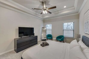 Une chambre à coucher comprenant un lit, un téléviseur, une commode, deux chaises et un ventilateur de plafond.