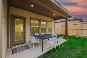 Une terrasse couverte avec une table et des chaises, une porte avec un panneau de verre et, au fond, une clôture en bois.