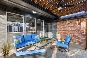 An outdoor patio with a blue sofa, a glass table, and a brick wall. - Luxury Backyard Pool & Patio Oasis (Lewisville)
