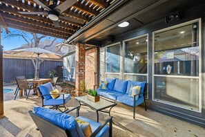 An outdoor patio with a brick wall, blue furniture, and a pergola. - Luxury Backyard Pool & Patio Oasis (Lewisville)