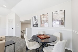 A room with a round table, white chairs, a chessboard, and three movie posters on the wall. - Luxury Backyard Pool & Patio Oasis (Lewisville)