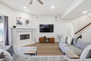 A modern living room with a fireplace, a flat-screen TV, and a staircase. - Luxury Backyard Pool & Patio Oasis (Lewisville)