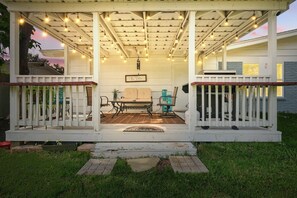 A covered porch with string lights, a table and chairs, and a sign reading 'The Patio.' - Charming 3-bed/2-bath Hidden Gem w Yard (Richardson)
