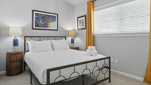 Una camera da letto con un letto, due comodini con lampade, una finestra con persiane e un'opera d'arte appesa al muro.