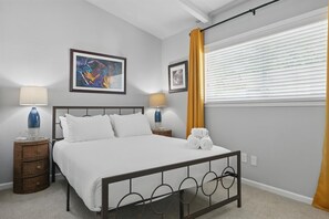 A bedroom with a bed, two bedside tables with lamps, a window with blinds, and artwork on the wall. - Charming 3-bed/2-bath Hidden Gem w Yard (Richardson)