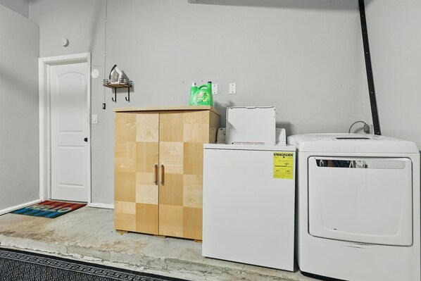 A laundry room with a wooden cabinet, a washing machine, and a dryer. - Charming 3-bed/2-bath Hidden Gem w Yard (Richardson)