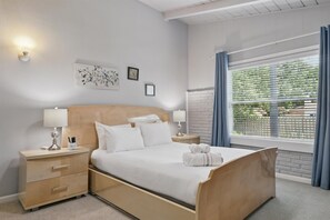 A neatly arranged hotel room with a bed, bedside tables, a nightstand, a window with curtains, and a wall-mounted light fixture. - Charming 3-bed/2-bath Hidden Gem w Yard (Richardson)
