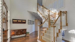 A spacious hallway with a wooden staircase, a built-in bench, and a wall-mounted shelf with framed pictures. - Gorgeous Vacation Home w/ Private Pool (Mesquite)