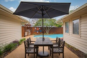 A patio with a table and chairs, a pool, and a wooden fence in the background. - Best of Richardson 5bd/3ba With Pool, Patio, BBQ (Richardson)