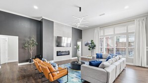 A modern living room with a grey sofa, a brown leather chair, and a TV mounted on the wall. - 5-bd/2-ba Vacation Retreat w/ Pool, Hot Tub & bbq (Fort Worth)